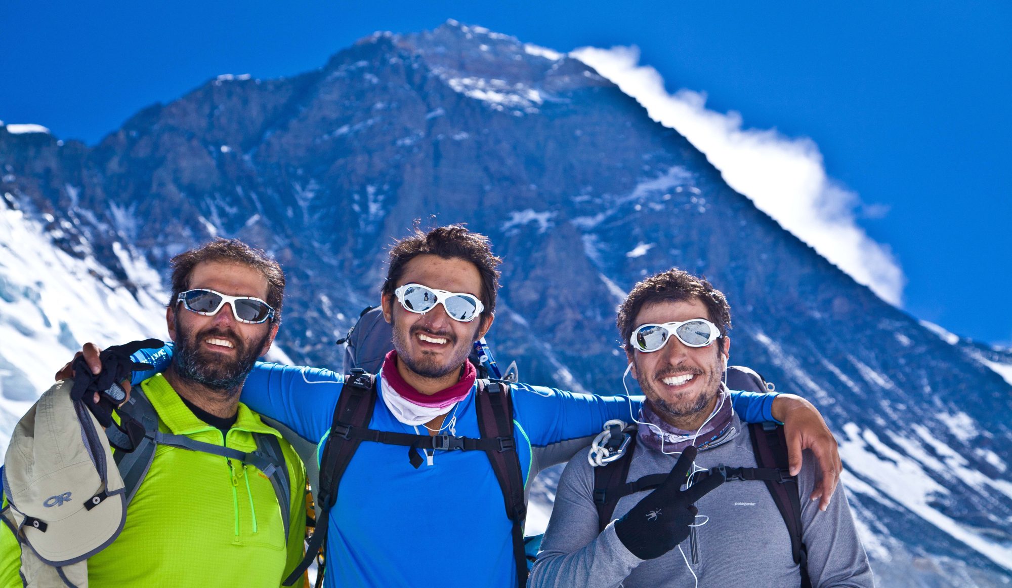 Three climbers smiling in front of a vast peak
