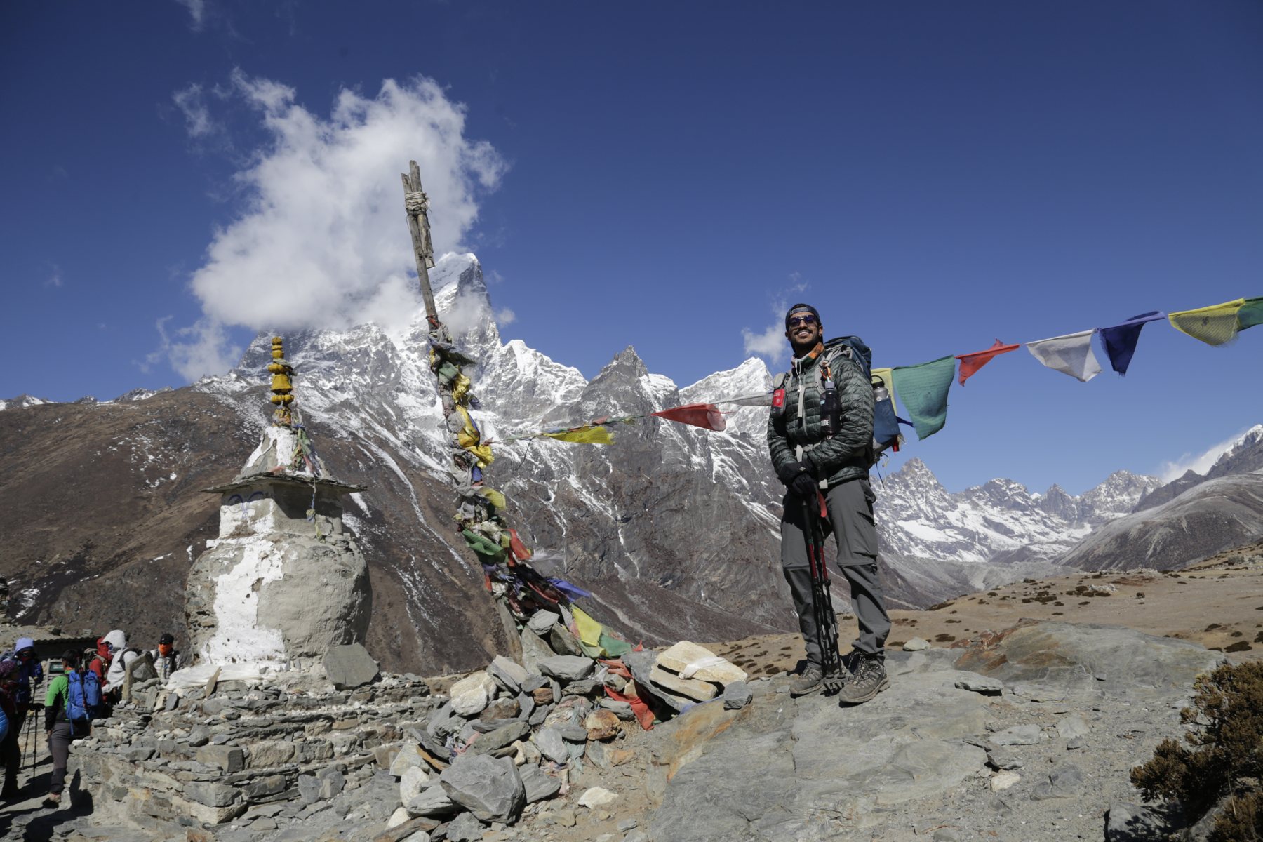 A smiling trekker beneath prayer flags and dramatic Himalayan peaks