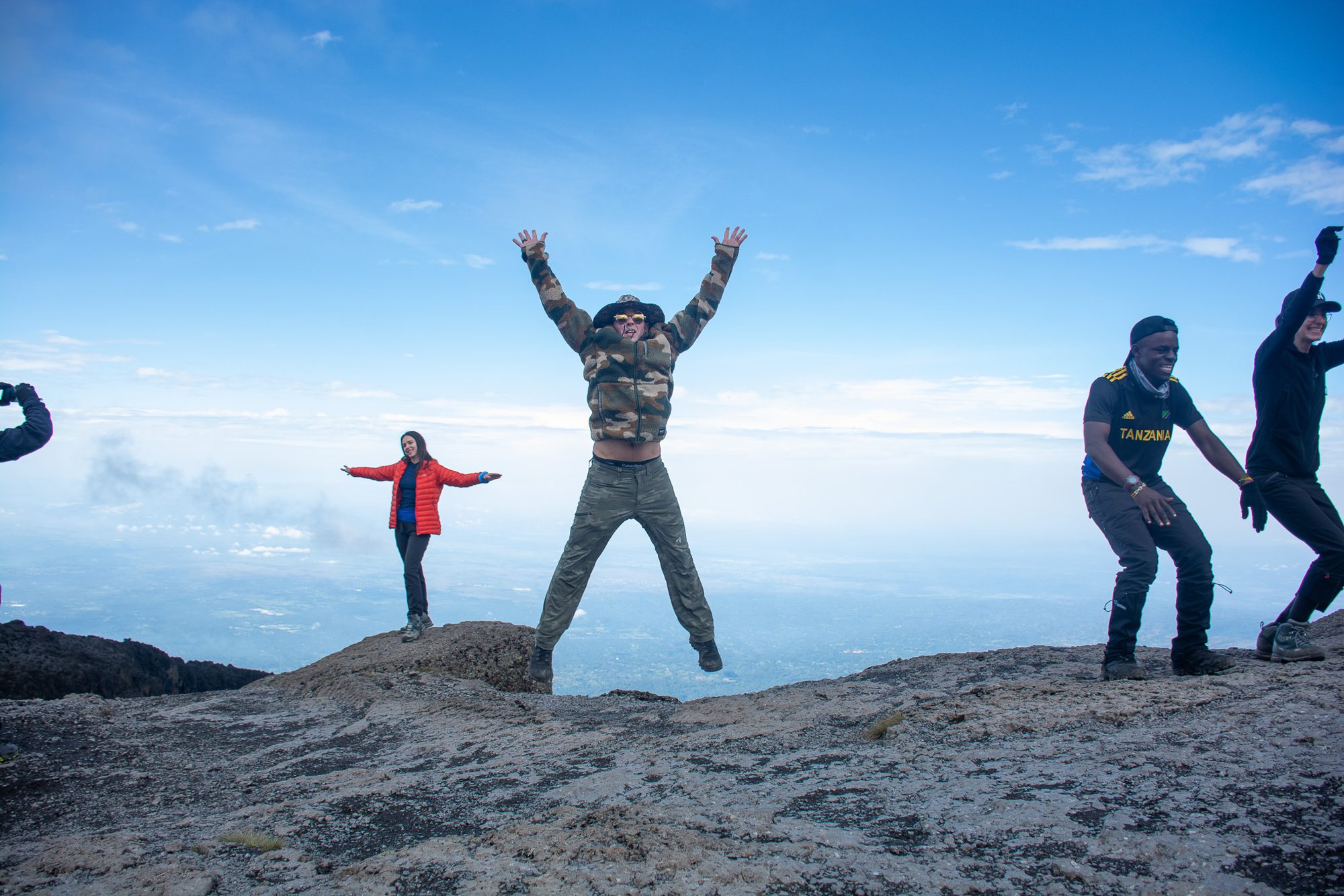 Climbers jumping for joy on a rock above the clouds