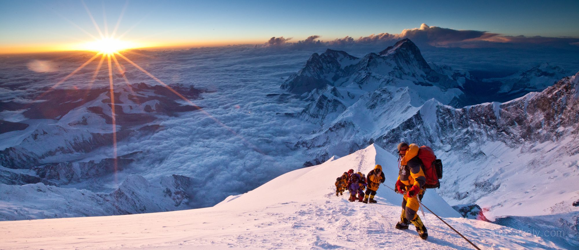 Climbers on a snow ridge at sunrise above the clouds