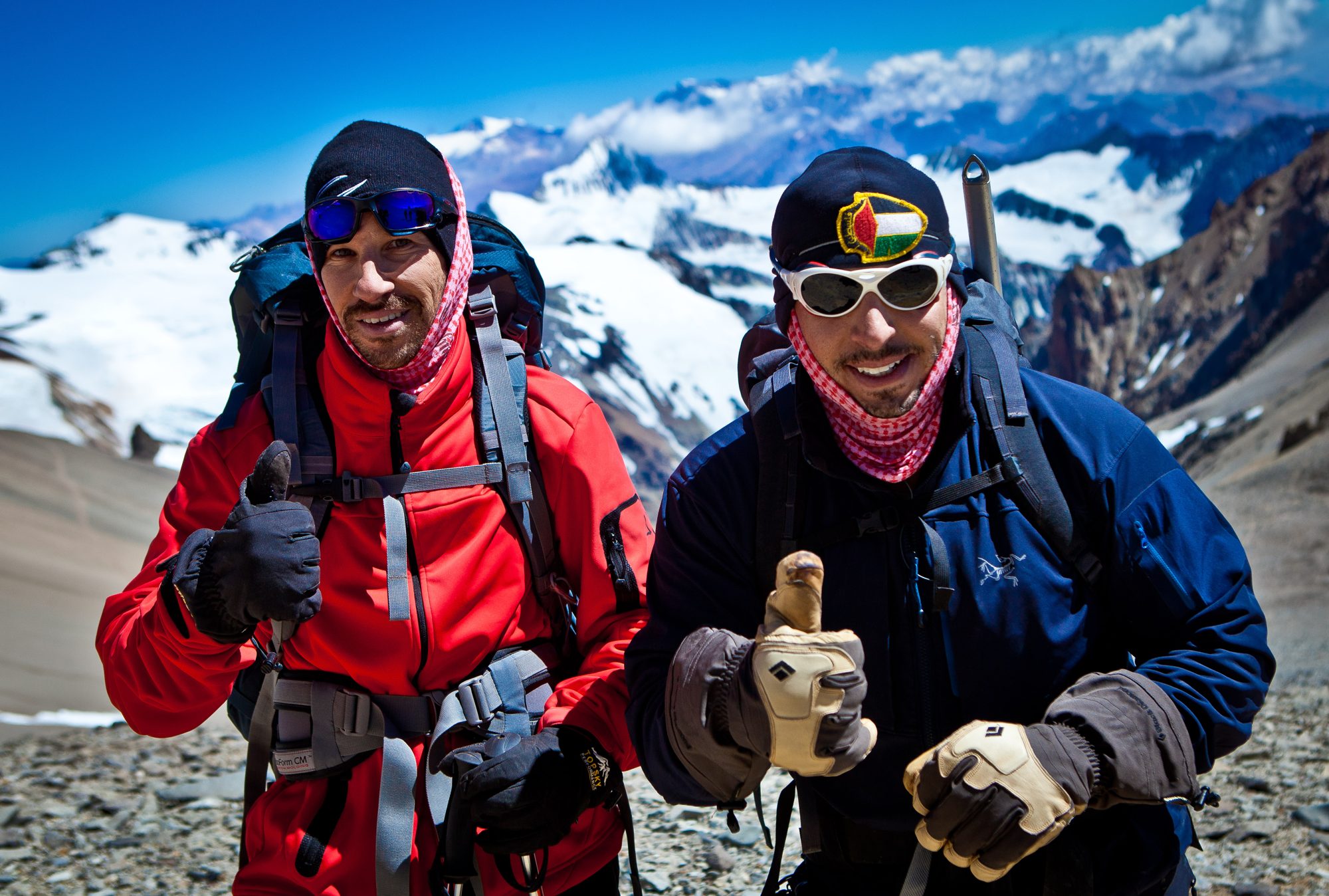 Two climbers with thumbs up in front of snowy mountains