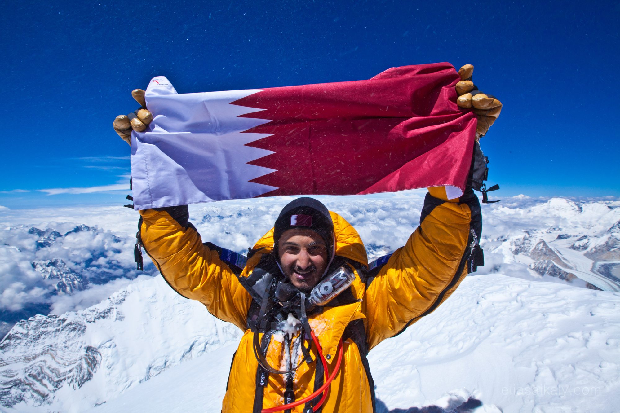 Moe holding the Qatar flag above a sea of cloud