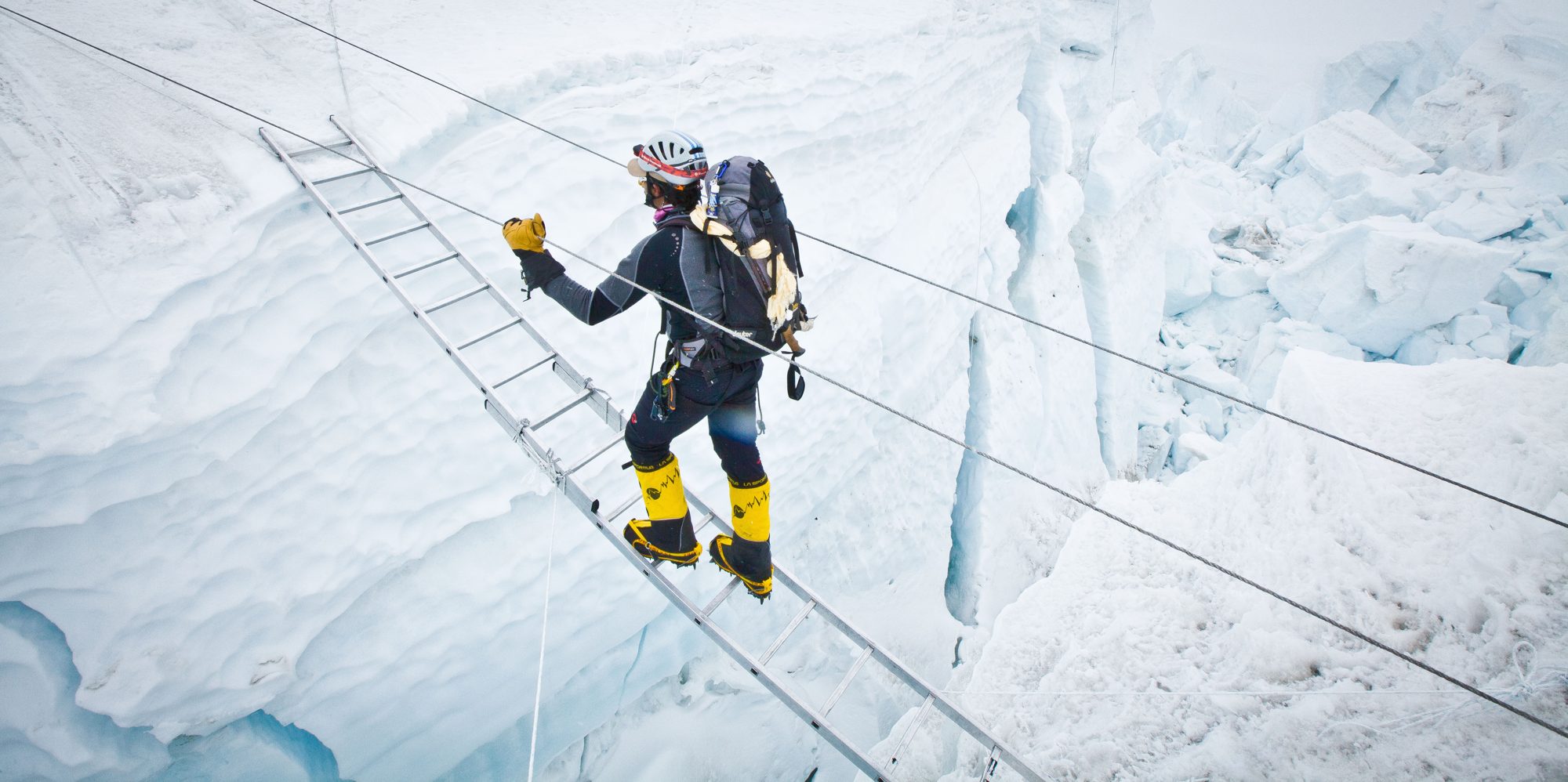 A climber crossing a ladder over a crevasse
