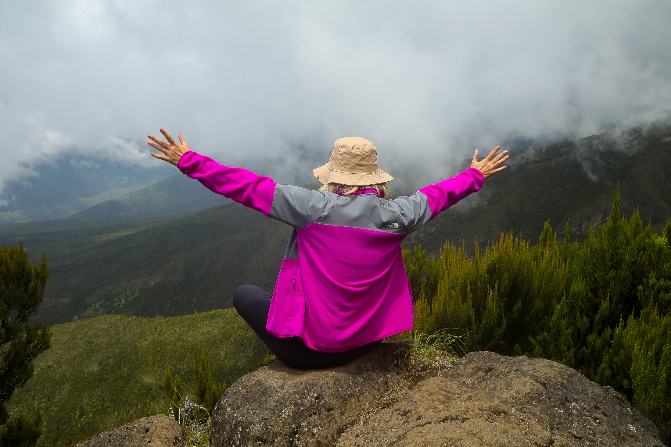 A climber with arms open wide on a rock above the valley