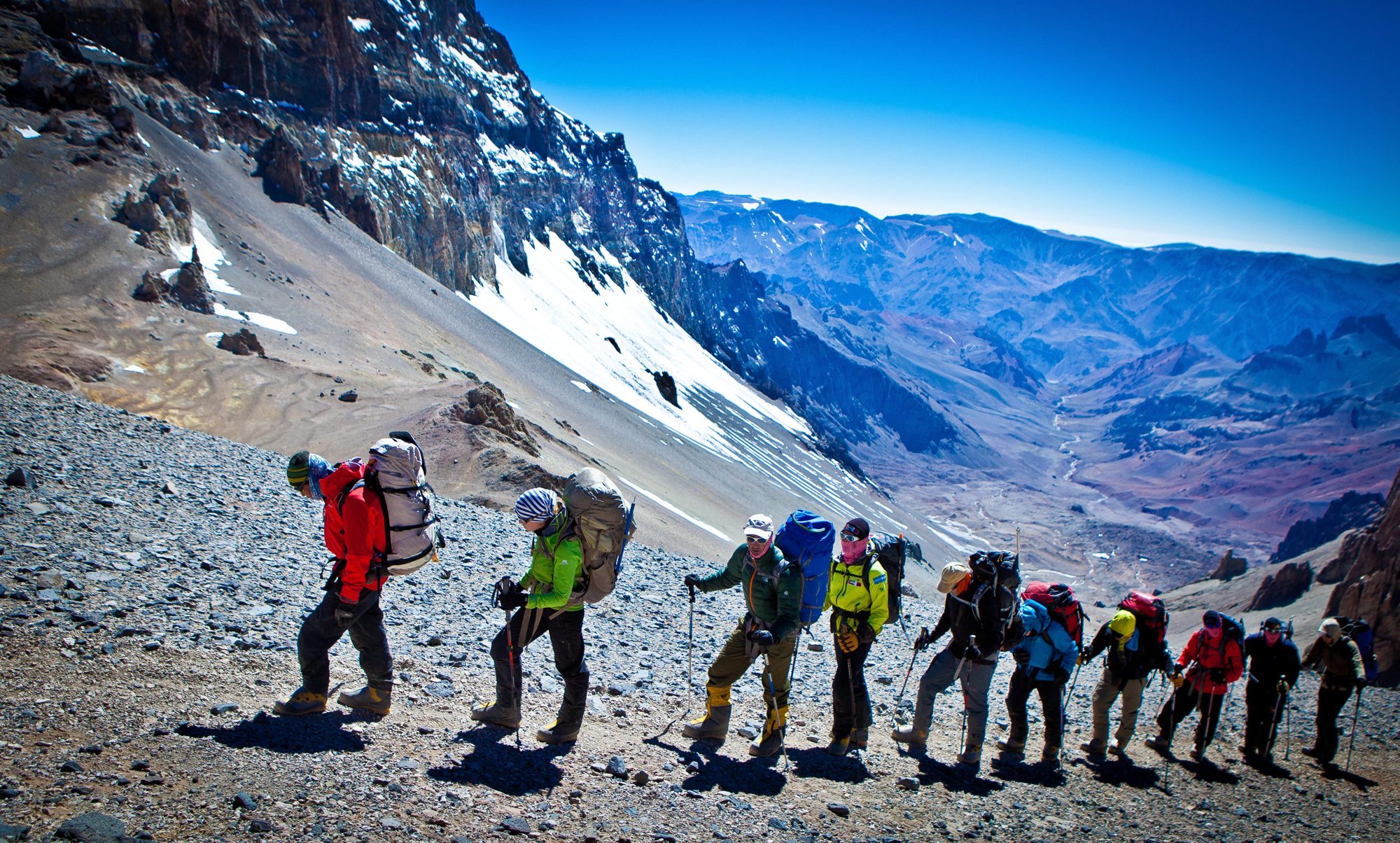 A long line of climbers on a rocky high-altitude slope