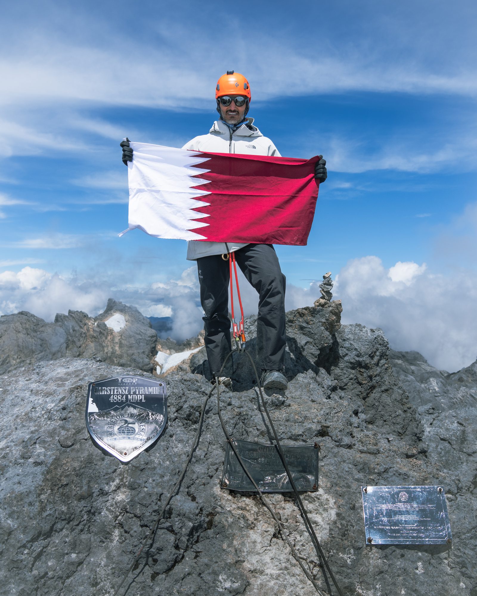 Moe holding the Qatar flag at the summit of Carstensz Pyramid