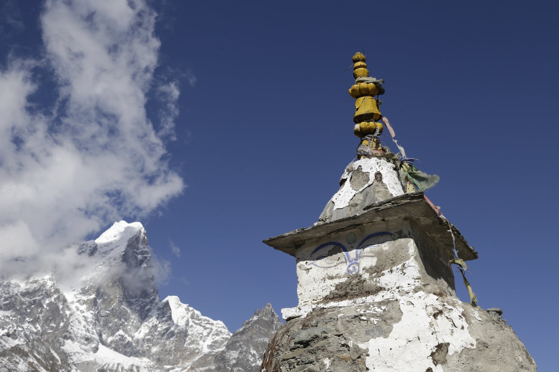 A golden-topped stone monument framed by mountain peaks and drifting clouds